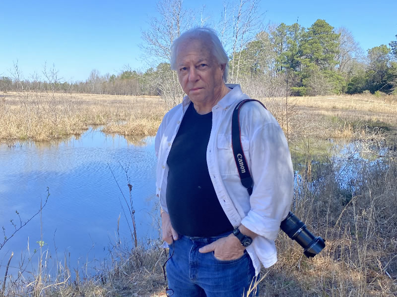 Photograph of author Tom Poland standing by a marshy pond.