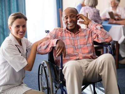 Smiling senior man in a wheelchair with a smiling nurse kneeling next to him.