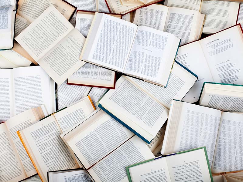 A large number of books open on a table, their text visible.