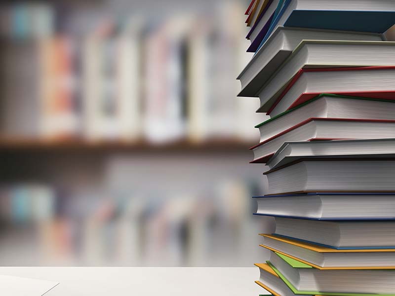 Stack of books on a table, blurry library shelves behind in the distance.