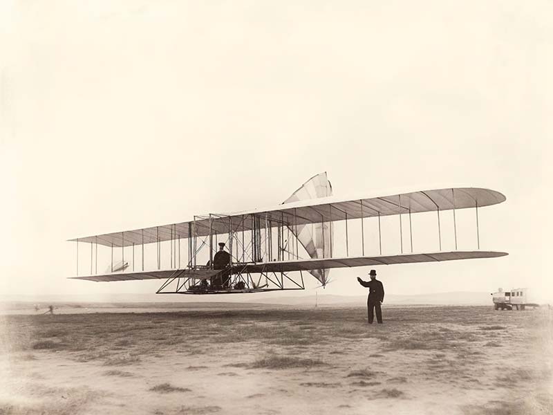 A photo of the Wright Brothers with their plane. Black and white.