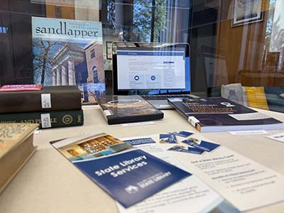 Display case showing library cards, computer screen with Library Card Sign-up, and various brochures. page