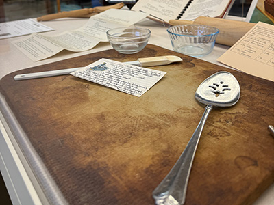 A serving spoon and recipe card on a wooden cutting board in the State Library display case.