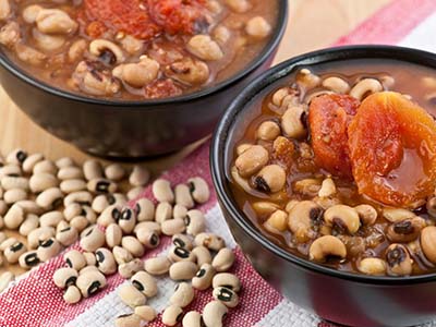 Black eyed peas and stewed tomatoes in a bowl on a checkered table cloth.