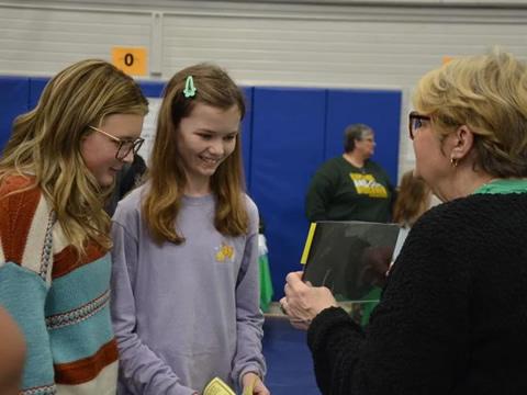 Two students are shown a book by a teacher.