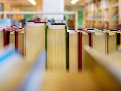 Library books on a shelf with further books seen in the distance