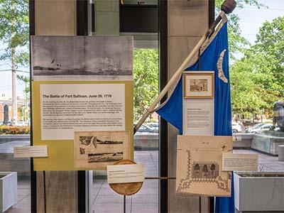 Items onm display in our lobby including a old state flag, info on the Battle of Fort Sullivan, and a piece of the palmetto log fort.