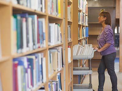 A photo of a librarian pushing a book cart between library stacks.