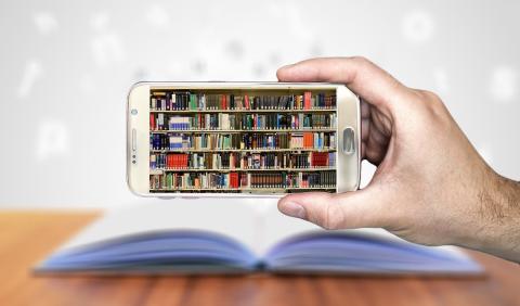 Hand holding a smart phone that shows a photo of a stack of library books. 