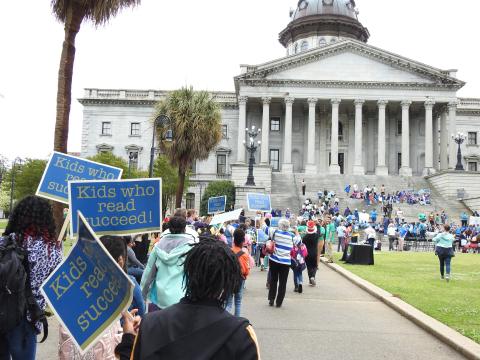 Kids walking to the State House holding signs that say, "Kids Who Read Succeed."