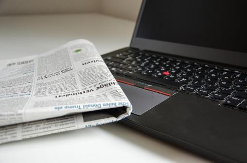 A newspaper rests atop a laptop computer. 