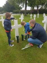 Photo of two young boys and their father placing flowers at a gravesite.