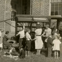 black and white image of an early bookmobile with children and librarians