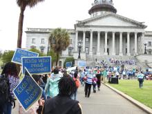 Kids walking to the State House holding signs that say, "Kids Who Read Succeed."