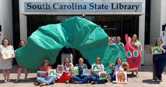 staff members holding up giant green caterpillar and eric carle books